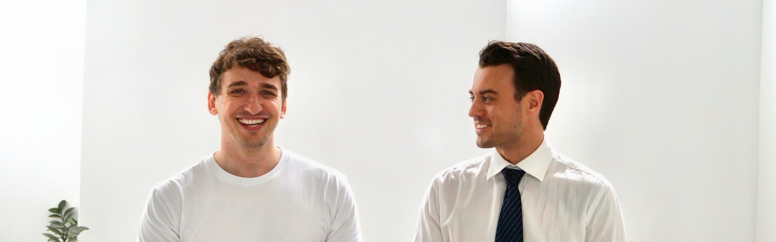 Johannes Freyer und Torben Lange stehen lachend an einem Tisch im Büro