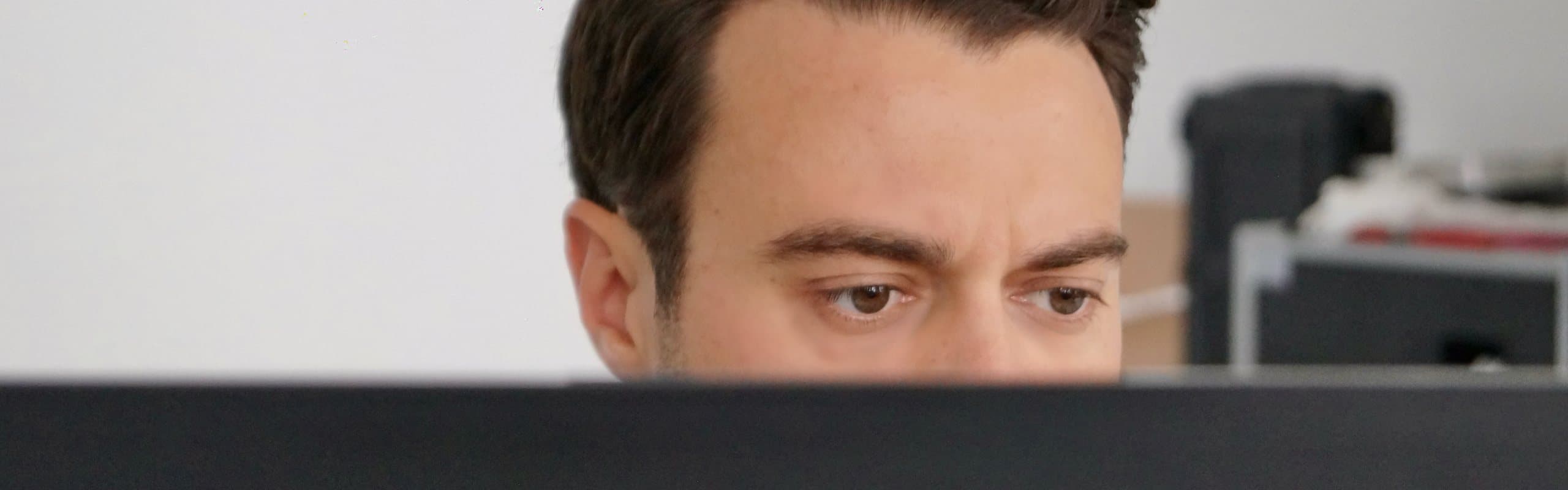 Torben Lange blickt konzentriert über die Oberkante eines aufgeklappten Laptops
